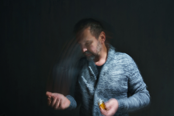 A mature man taking drug pill on dark background, mental health concept.