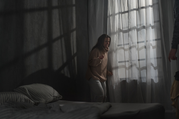 A scared woman standing next window with fear from her violent husband at home.