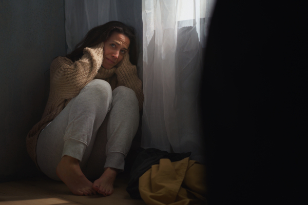 A scared woman sitting on ground and covering her head in fear of domestic violence.