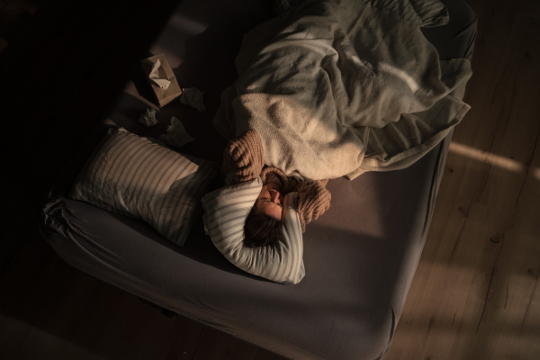 An overhead view of sad woman suffering from multiple personality disorders lying in bed.