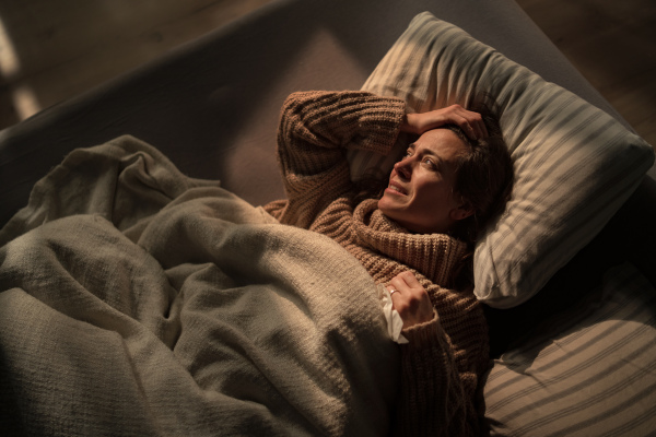 A sad woman suffering from depression lying in bed in night.