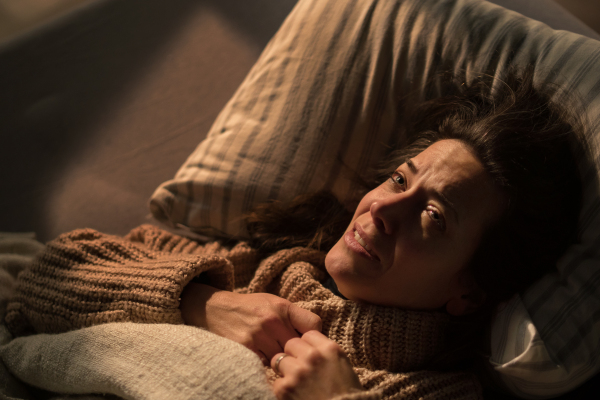 A close-up of sad woman suffering from covid depression lying in bed in night.