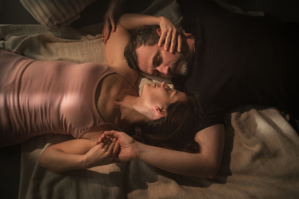 An overhead view of mid-adult couple lying in bed at night and hugging and looking at each other.