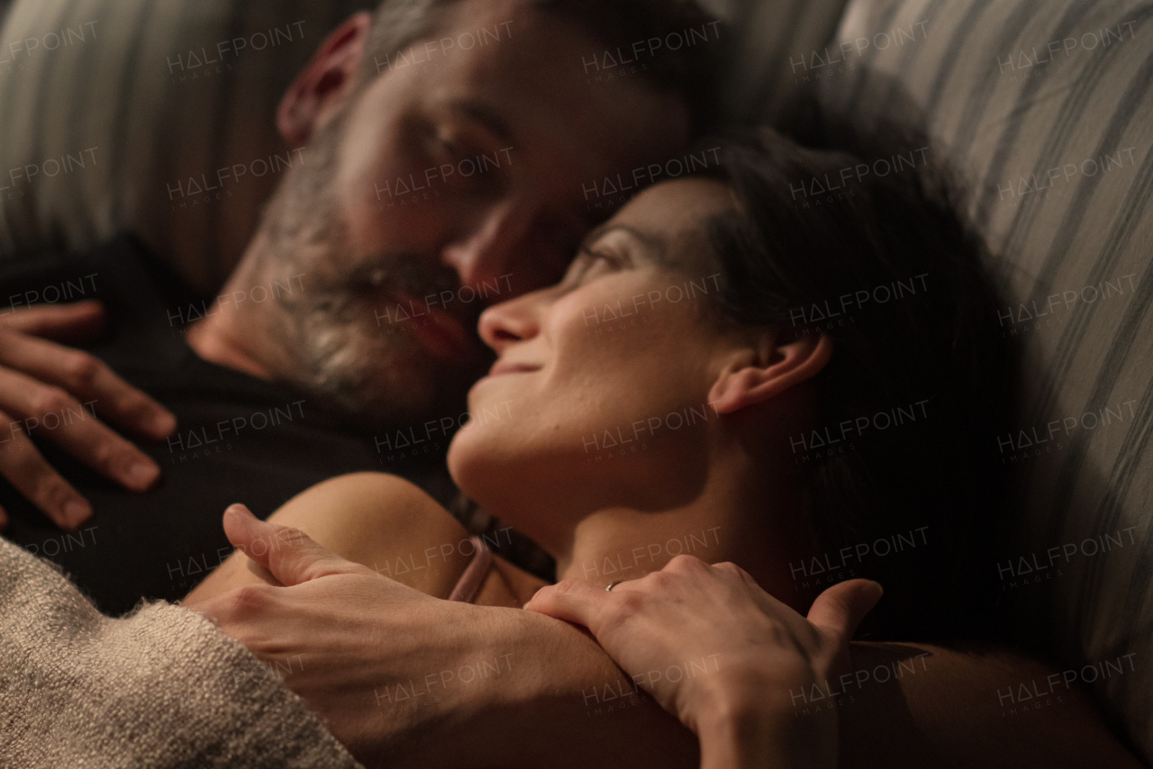 A close-up of mid-adult couple lying in bed at night and hugging and looking at each other.