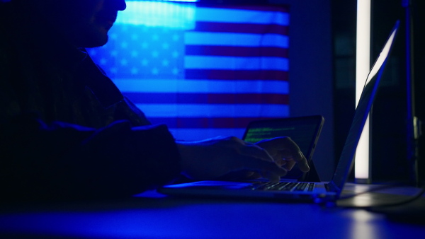 A hacker with laptop and USA flag in background. Cyber attack concept.