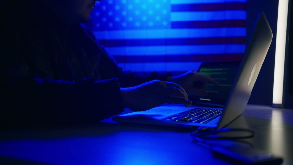 A hacker with laptop and USA flag in background. Cyber attack concept.