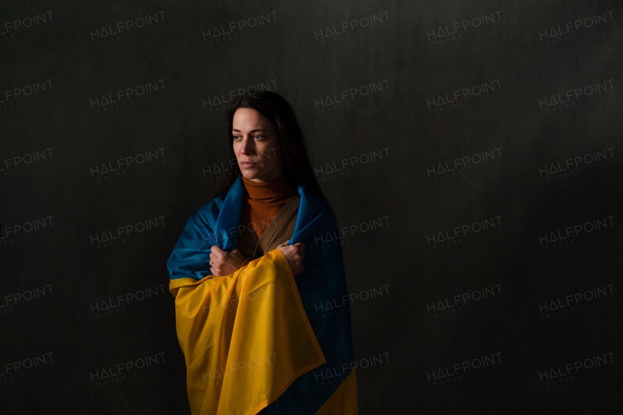 A sad woman covered with Ukraine flag. Concept of standing with Ukrainian nation in war with Russia.