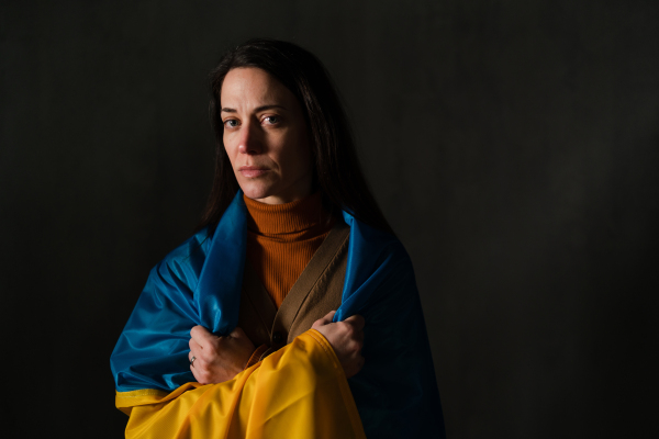 A sad woman covered with Ukraine flag. Concept of standing with Ukrainian nation in war with Russia.