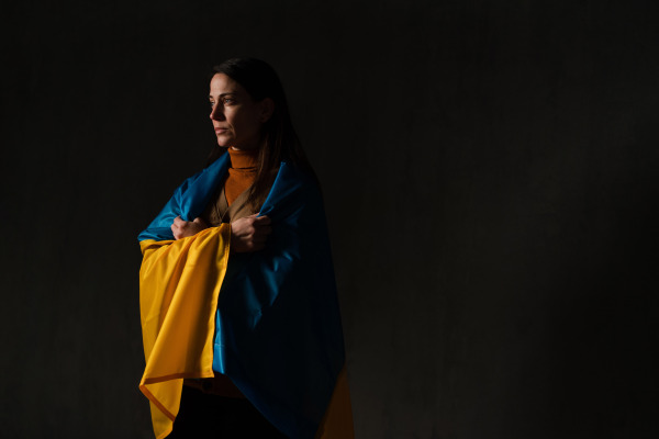 A sad woman covered with Ukraine flag. Concept of standing with Ukrainian nation in war with Russia.