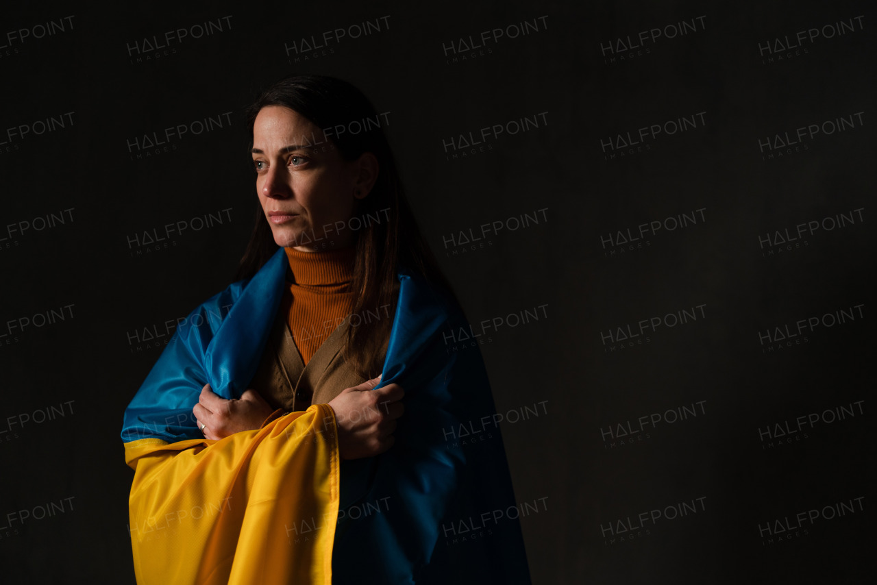 A sad woman covered with Ukraine flag. Concept of standing with Ukrainian nation in war with Russia.