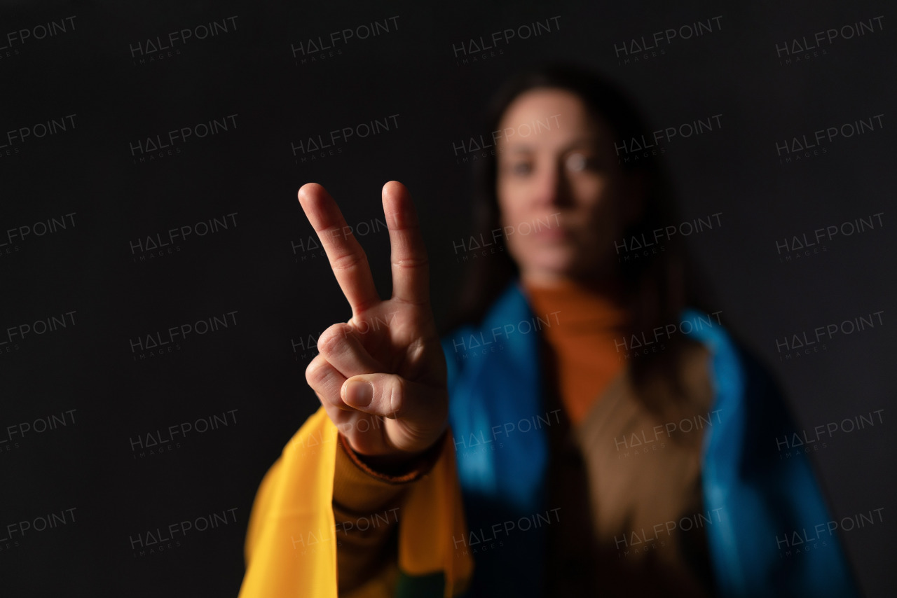 A sad woman covered with Ukraine flag showing peace sign. Concept of standing with Ukrainian nation in war with Russia.