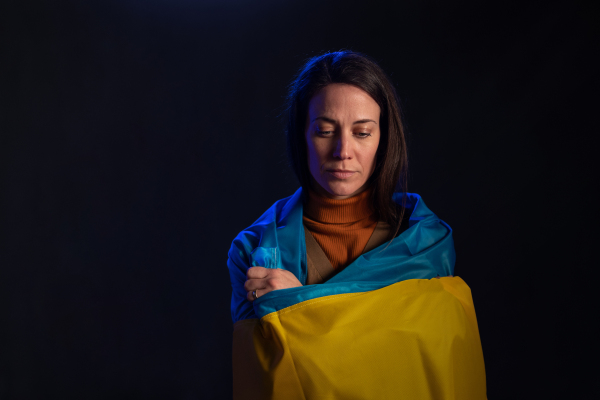 A sad woman covered with Ukraine flag. Concept of standing with Ukrainian nation in war with Russia.