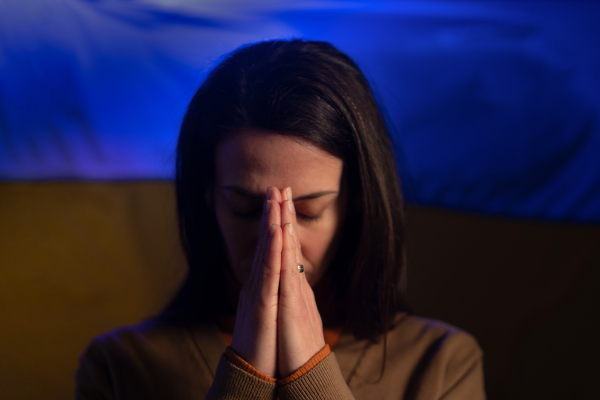 A sad woman with Ukraine flag at background praying. Concept of standing with Ukrainian nation in war with Russia.