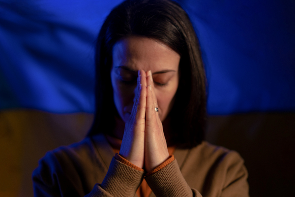 A sad woman with Ukraine flag at background praying. Concept of standing with Ukrainian nation in war with Russia.