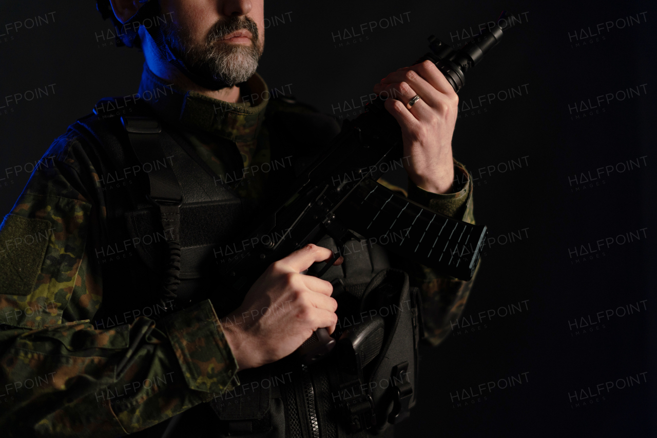 A close-up of soldier in military uniform with weapon on black background.