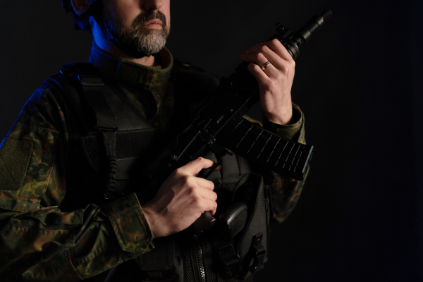 A close-up of soldier in military uniform with weapon on black background.