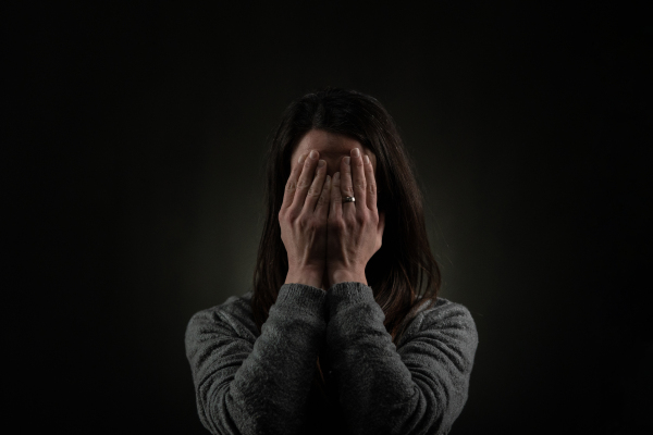 A depressed mid-adult woman, alone in darkness, covering her face with hands, mental health concept.