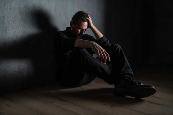 A sad mature man, alone in darkness, sitting and thinking.