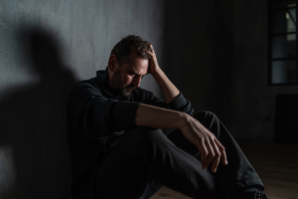 A sad mature man, alone in darkness, sitting and thinking.