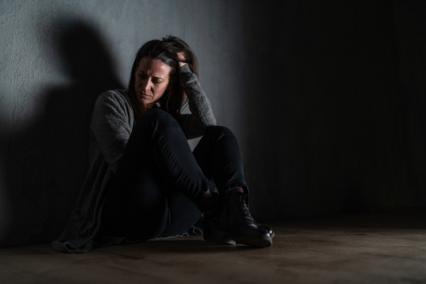 A sad mid-adult woman, alone in darkness, sitting and thinking.