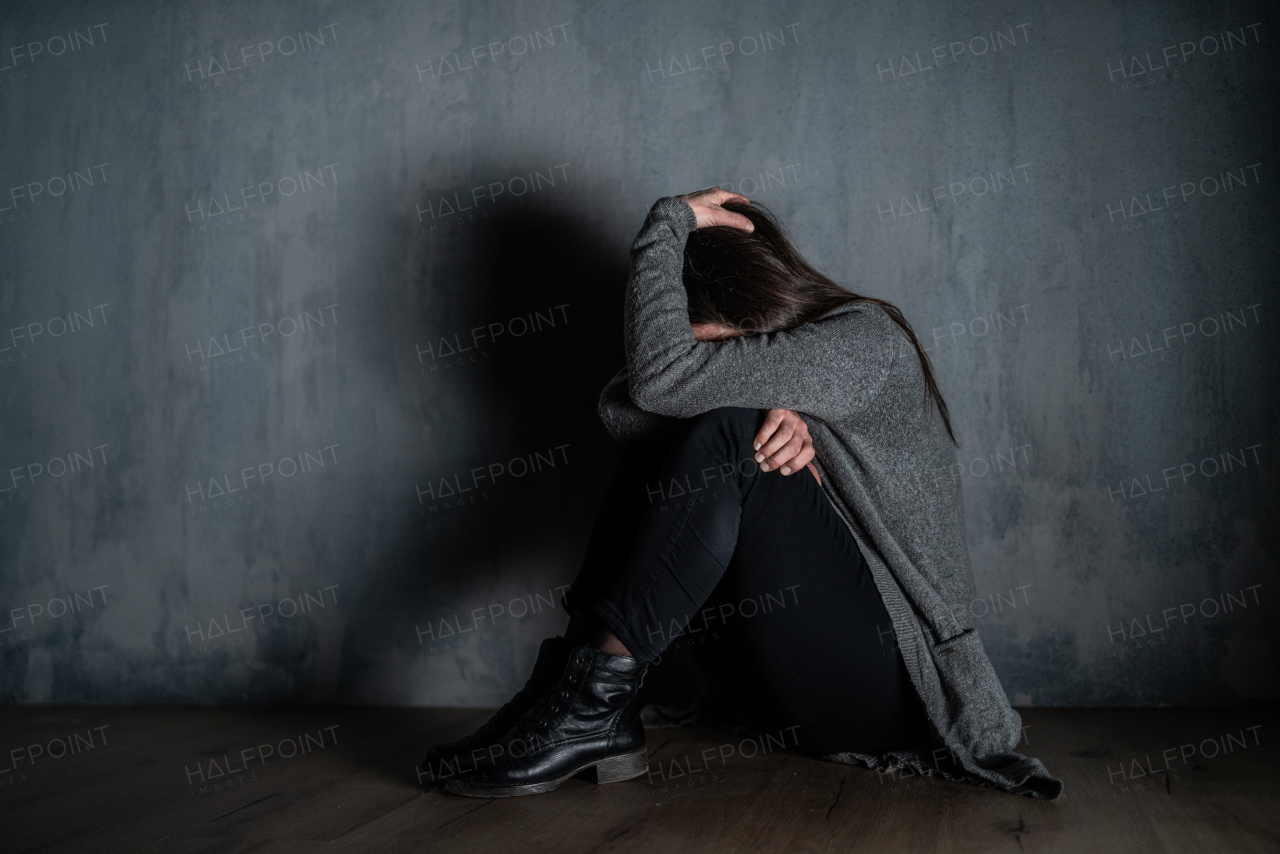 A sad mid-adult woman, alone in darkness, sitting and thinking.