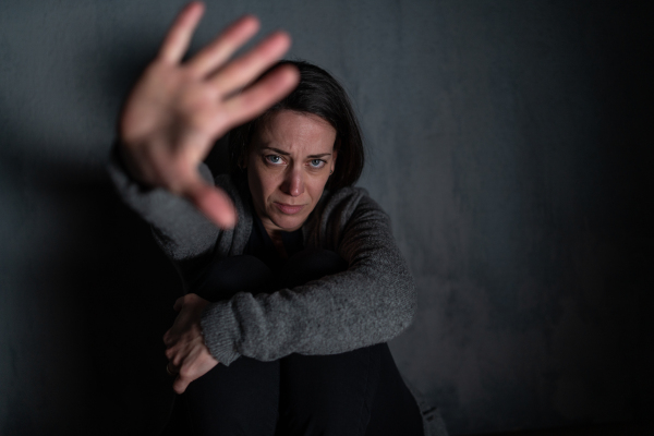 A depressed mid-adult woman, alone in darkness, looking at camera, stop the war concept.