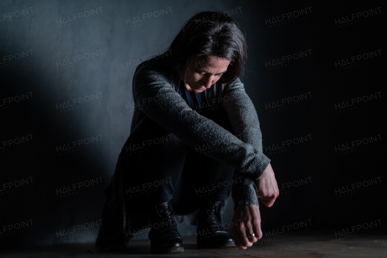 A sad mid-adult woman, alone in darkness, sitting and thinking.