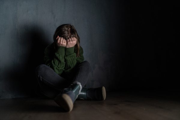 A sad little girl, alone in darkness, sitting and and covering face.