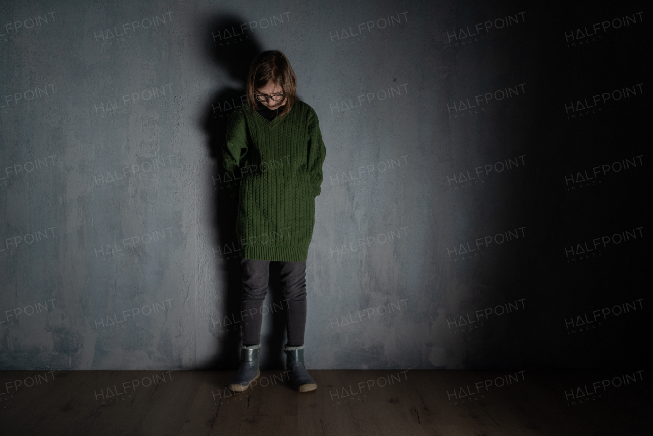 A sad little girl, alone in darkness, standing and thinking.