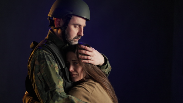 A sad woman hugging her military husband and saying-goodby to him before going to army on black backgound.