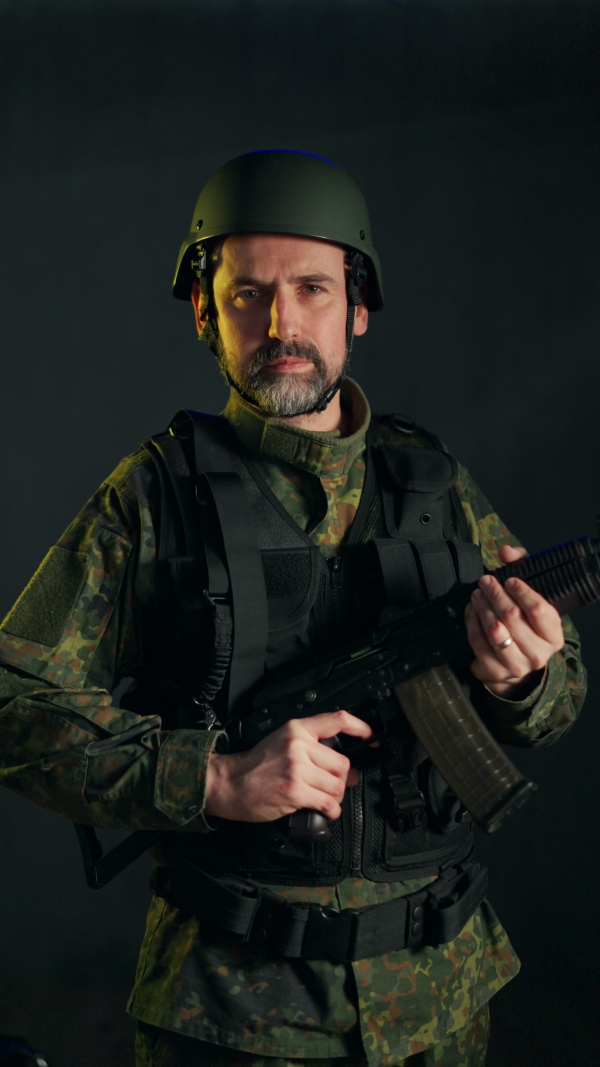 An Ukrainian soldier in military uniform holding weapon on black background.