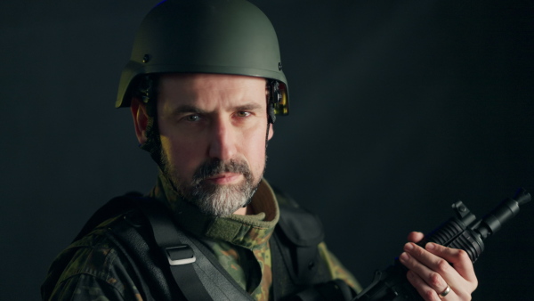 A close-up of Ukrainian soldier in military uniform and helmet looking at camera on black background.