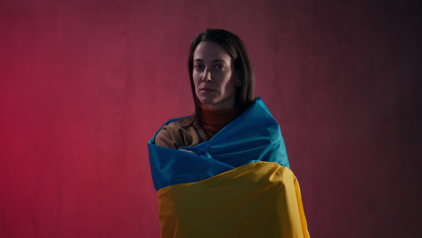 A sad woman covered with Ukraine flag. Concept of standing with Ukrainian nation in war with Russia.