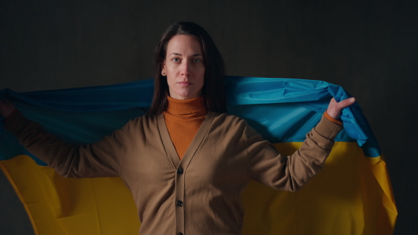 A sad woman covering with Ukrainian flag. Concept of standing with Ukrainian nation in war with Russia.