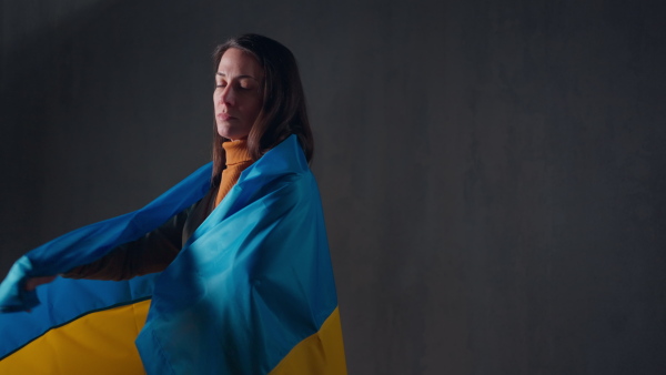 A sad woman covering with Ukrainian flag. Concept of standing with Ukrainian nation in war with Russia.