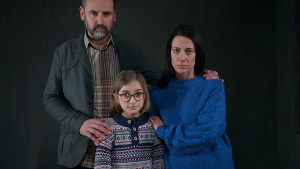 A refugee family with one child looking at camera on black background, Ukraine war concept.