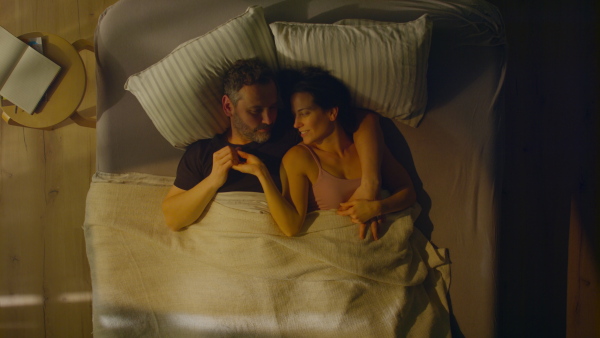 An overhead view of mid-adult couple lying in bed at night and hugging and looking at camera.