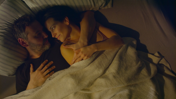 An overhead view of mid-adult couple lying in bed at night and hugging