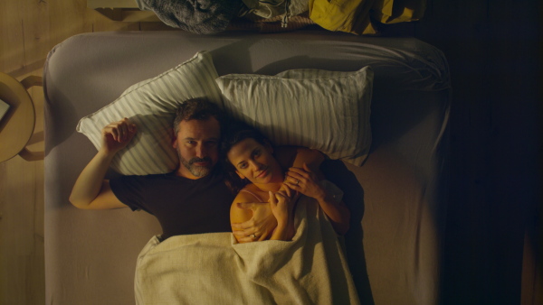 An overhead view of mid-adult couple lying in bed at night and hugging and looking at camera.