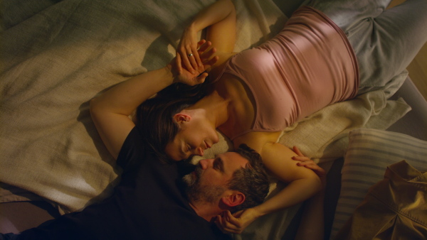 An overhead view of mid-adult couple lying in bed at night and hugging and looking at each other.