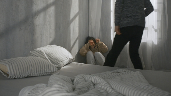 A scared woman sitting in corner with fear from her violent husband at home.