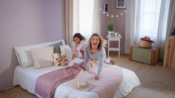 A happy mother with her little daughter lying on bed and reading book at home.