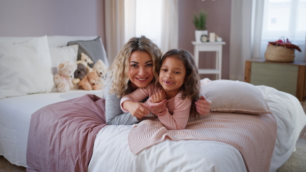 A happy mother with her little daughter lying on bed and looking at camera at home.