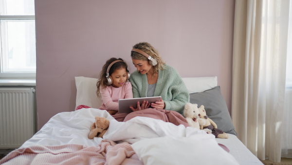 A happy mother with her little daughter lying on bed and using tablet at home.