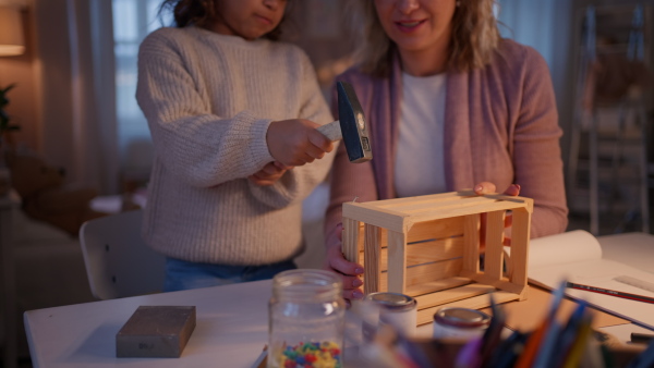 A happy little girl renovating a wooden crate together with her mother at home.