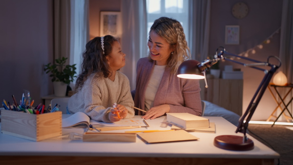 A little girl doing homework with her mother in evening at home.