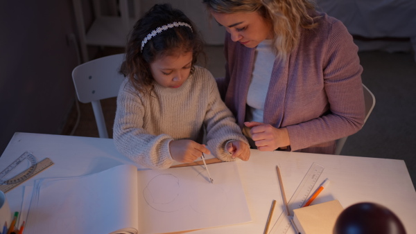 A mother helping her daughter with homework, drawing a circle with comasses in evening at home.