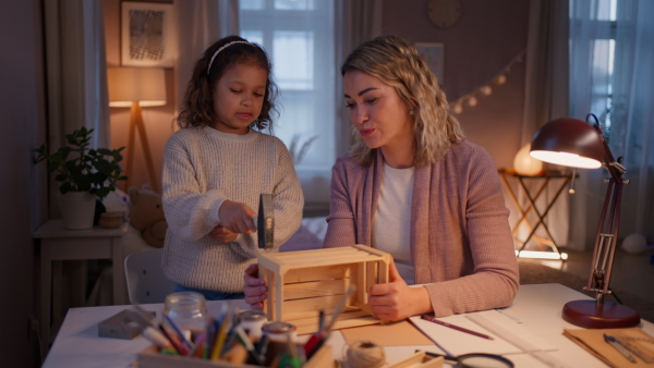 A happy little girl renovating a wooden crate together with her mother at home.