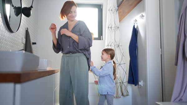 A little girl congratulates mother and gives her flower in bathroom at home.