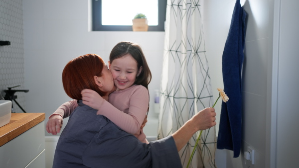 A little girl congratulates mother and gives her flower in bathroom at home.